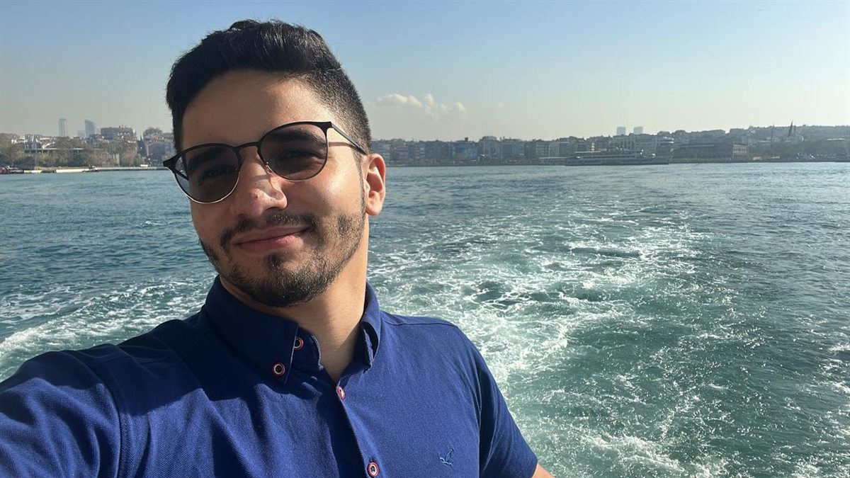 Ilyes smiling in sunglasses on a ferry, city skyline behind