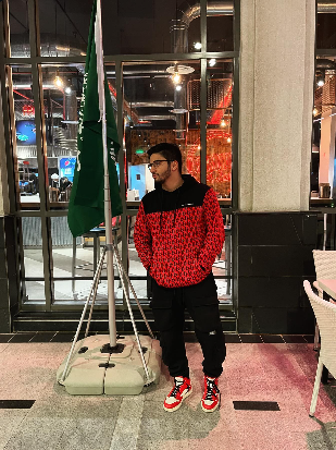 Ilyes standing next to a Saudi flag at night