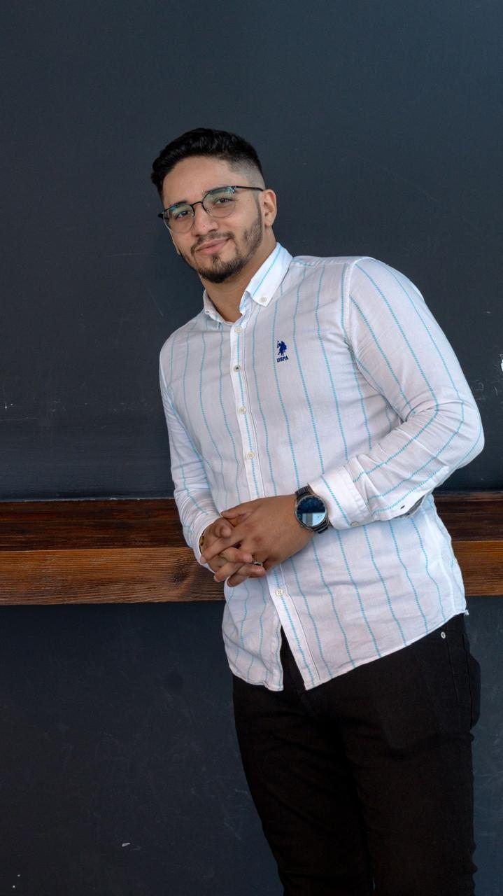 Ilyes in a striped shirt leaning against a wall, smiling